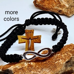 May include: Black braided bracelet with a silver infinity symbol charm and a wooden cross charm with the word "ENRI" engraved on it.