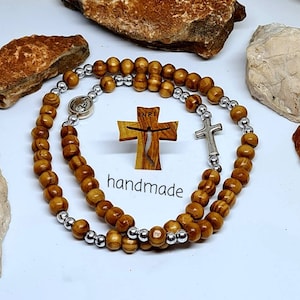 May include: A wooden rosary with brown beads and silver accents. The rosary features a wooden cross with the word "NRI" on it and a silver cross charm. The text "handmade" is visible in the image.