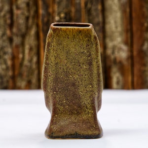 May include: A small, dark green and brown ceramic vase with a textured surface. The vase has a rectangular shape with rounded edges.
