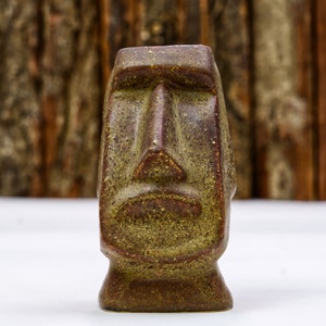 May include: A brown ceramic sculpture of a face with a textured surface. The face has a large nose and a closed mouth.