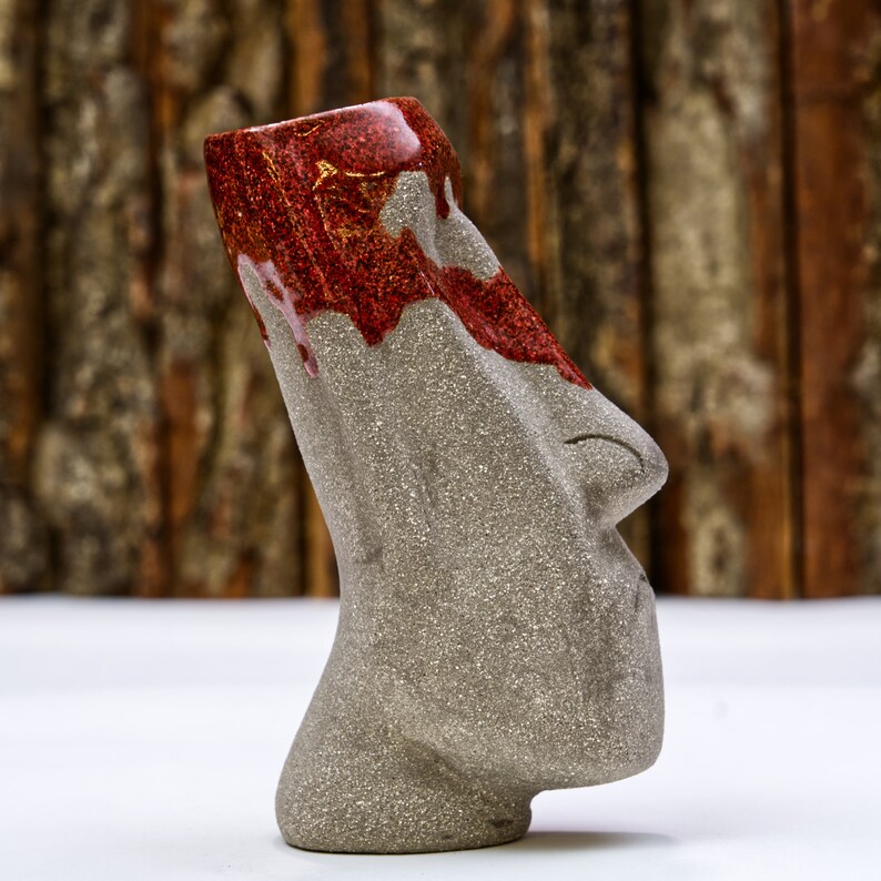 May include: A gray ceramic tiki mug with a red and gold glaze. The mug has a human-like face with a nose and mouth.