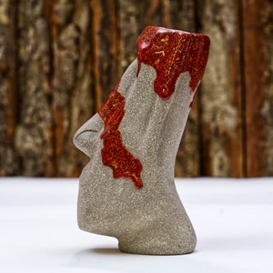 May include: A gray ceramic mug with a red and gold glaze. The mug is shaped like a face with a wide mouth and a pointed nose.