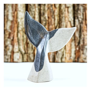 Può includere: Una scultura di coda di balena in ceramica con finitura grigia e bianca. La coda è curva e la base ha una forma conica arrotondata.