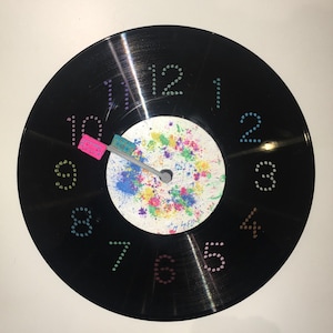 May include: A white ceramic mug with a black handle and the text "But First, Coffee" in a bold, black font. The mug is set against a blurred background, highlighting its clean design.