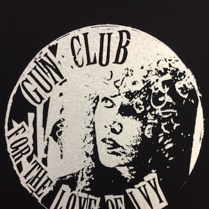 May include: A black and white circular design with the text "GUN CLUB FOR THE LOVE OF IVY" around the edge. A woman's face is in the centre of the design.