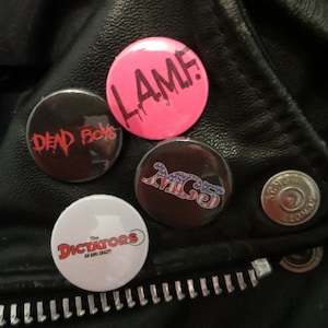 Może przedstawiać: Cztery okrągłe czarno-białe guziki z nazwami zespołów na czarnej skórzanej kurtce. Guziki przedstawiają napisy "Dead Boys", "The Dictators Go Girl Crazy", "MC5" i "Lame".