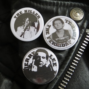 May include: Three black and white button pins featuring portraits of men. The top pin reads "The Killer" and features a man with a microphone. The middle pin reads "The Friday" and features a man with a police mugshot. The bottom pin reads "Terry Lee" and features a man with his middle finger raised.