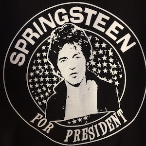 Op de afbeelding: Zwart-witte afbeelding van Bruce Springsteen met de tekst "Springsteen for President" in een cirkel.