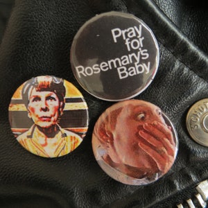 May include: Three round pinback buttons with different designs. One button has the text "Pray for Rosemary's Baby" on a black background. Another features a portrait. The third has a close-up image of a face.