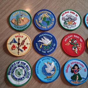 Pu&ograve; includere: Una collezione di toppe ricamate colorate con vari disegni. Alcune toppe presentano testi come "Gore Camp Scherman", "Friendships Around the World" e "Holiday Sing '92". Altre raffigurano immagini di animali e scene.