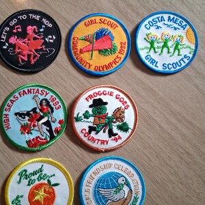 Pu&ograve; includere: Una collezione di toppe colorate delle Girl Scout. I disegni includono una figura danzante, una bandiera, tre figure verdi, una donna con una balena, una rana, un pomodoro e una colomba. Testi: "Let's Go To The Hop", "Girl Scout", "Costa Mesa Girl Scouts", "High Seas Fantasy", "Froggie Goes Country".