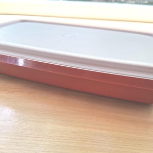 Op de afbeelding: Een rechthoekige, rode plastic container met een wit deksel. De container heeft een licht verhoogde rand en een gladde, glanzende afwerking. Het deksel past perfect op de bovenkant en creëert een luchtdichte afsluiting. De container is ontworpen voor voedselopslag.