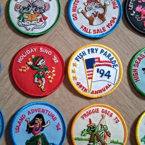 Pu&ograve; includere: Una collezione di toppe ricamate con vari disegni e testo. Le toppe presentano immagini di animali, persone e testo come "Holiday Sing", "Go Nuts for Girl Scouting" e "Island Adventure". Le toppe sono circolari con bordi colorati.
