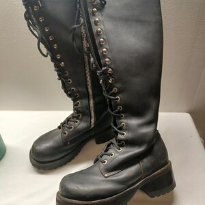 May include: A pair of black knee-high boots with a lace-up design and a chunky platform sole. The boots feature a zipper closure and metal eyelets. The boots are made of a leather-like material.