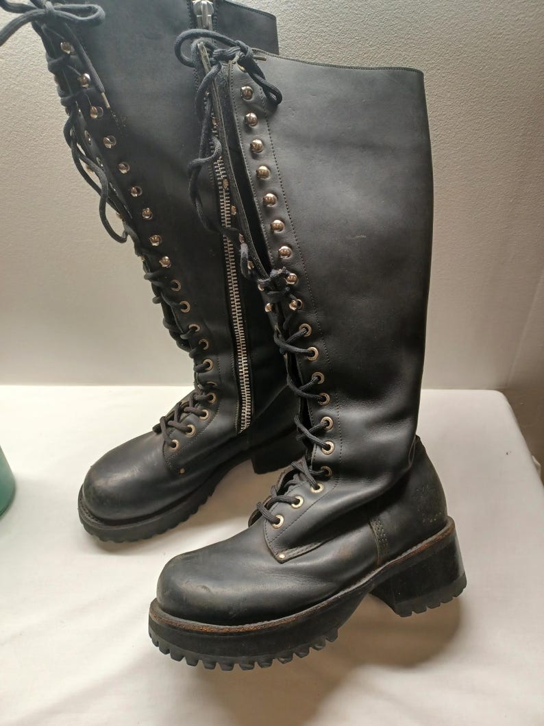 May include: A pair of black knee-high boots with a lace-up design and a chunky platform sole. The boots feature a zipper closure and metal eyelets. The boots are made of a leather-like material.