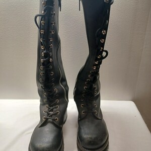 May include: A pair of black knee-high boots with a lace-up design and side zippers. The boots have a rugged sole and metal eyelets. The laces are black, and the zippers are silver.