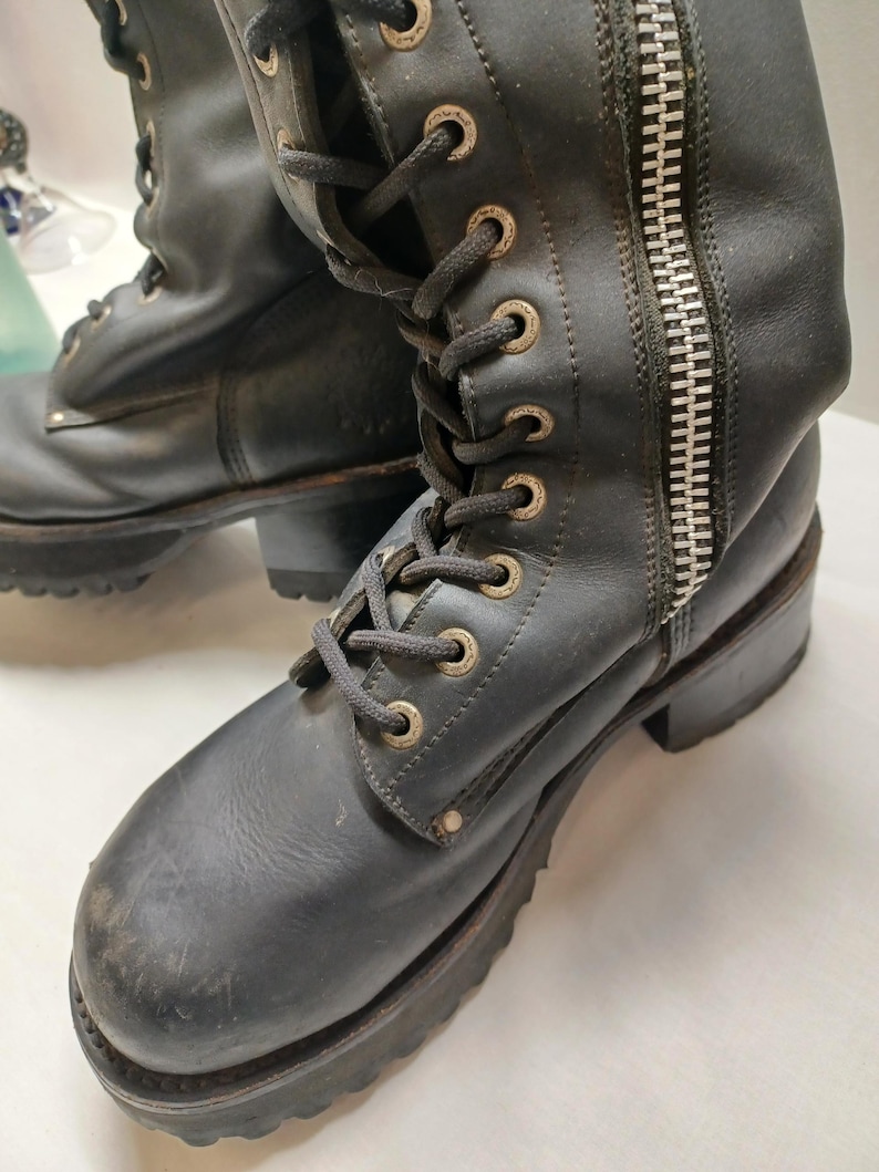 May include: Black leather boots with a lace-up front and a side zipper. The boots have a chunky sole and metal eyelets. The boots appear worn, with scuffs and marks on the leather.