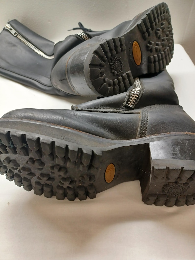 May include: Pair of black leather boots with chunky soles and side zippers. The boots have a rugged, worn appearance, with visible wear on the soles and uppers. The soles have a deep tread pattern for traction. The boots are likely for outdoor or work wear.