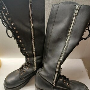 May include: A pair of black leather knee-high boots. Each boot features a full-length silver zipper on the side and lace-up detailing. The boots have a lug sole and a round toe.