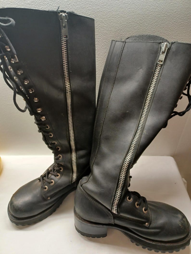 May include: A pair of black leather knee-high boots. Each boot features a full-length silver zipper on the side and lace-up detailing. The boots have a lug sole and a round toe.