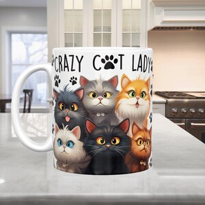 May include: White ceramic mug with a black paw print and the text "Crazy Cat Lady". The mug features a colorful illustration of six cats with different fur colors and patterns.