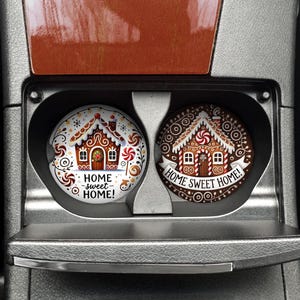 May include: Two round car coasters with gingerbread house designs. One is white with a colorful gingerbread house and the text "HOME sweet HOME!". The other is brown with a gingerbread house and the text "HOME SWEET HOME!".