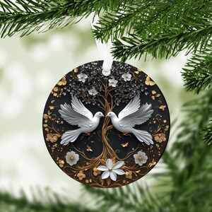 May include: Round Christmas ornament featuring a tree of life design with two white doves facing each other. The ornament has a black background with gold and white floral accents and a white ribbon for hanging.