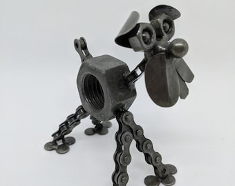 May include: A metal dog sculpture made from nuts, bolts, and chain links. The dog's body is a large nut, with chain links forming the legs and various metal pieces creating the head. A unique piece of industrial art.