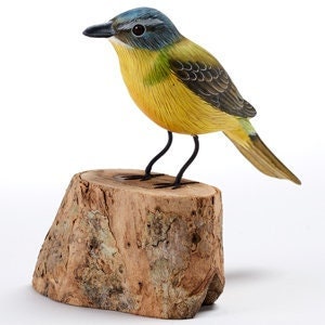 Puede incluir: Figurita de pájaro de madera tallada a mano, pintada en azul, amarillo y verde, posada sobre una base de madera natural.
