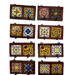Könnte beinhalten: Satz von acht Schlüsselhaken aus Holz mit jeweils zwei Haken. Jeder Haken ist mit zwei bunten Keramikfliesen mit Blumenmustern verziert. Die Fliesen sind in Blautönen, Gelb, Rosa, Rot und Grün.