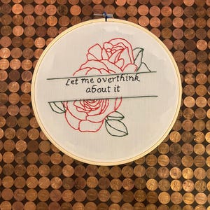 Puede incluir: Arte de bordado en aro con una rosa roja y hojas verdes. El texto "Let me overthink about it" está bordado en hilo negro.
