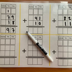 Puede incluir: Una pizarra blanca de borrado en seco con seis problemas de suma escritos con marcador negro. Los problemas están configurados en un formato de cuadrícula con columnas de cientos, decenas y unidades. Un marcador de borrado en seco blanco está sobre la pizarra.