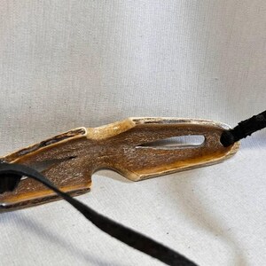 May include: A brown and tan antler eyeglass holder with a black strap. The holder has a unique shape with a cutout and is designed to hold eyeglasses. The black strap is attached to the holder.