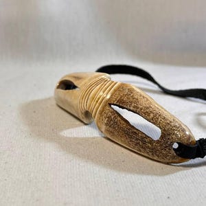 May include: A carved wooden pendant with a black cord. The pendant is light brown with a darker brown section and a white painted accent. The pendant has a hole carved through it.