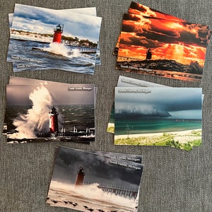 May include: A collection of postcards featuring the South Haven, Michigan lighthouse. Each postcard displays a different dramatic scene of the lighthouse, with stormy weather and crashing waves. The text "South Haven, Michigan" is printed on each card.