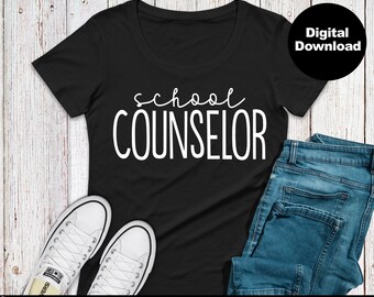 以下が含まれることがあります： 白い筆記体で「school counselor」と書かれた黒いTシャツ。Tシャツは木製の表面に置かれ、白いスニーカーと青いジーンズが置かれている。