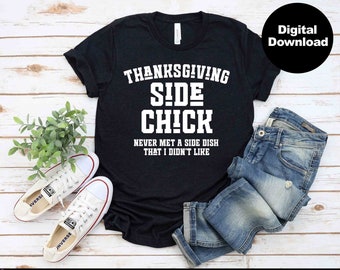 May include: A black t-shirt with the text "Thanksgiving Side Chick Never Met A Side Dish That I Didn't Like" in white. The shirt is laid out on a wooden surface with a pair of white sneakers, blue jeans, and a green plant.