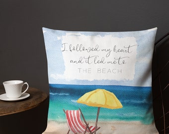 May include: A throw pillow with a watercolour beach scene. The pillow features a yellow umbrella, a red and white striped beach chair, and the text "I followed my heart and it led me to THE BEACH".