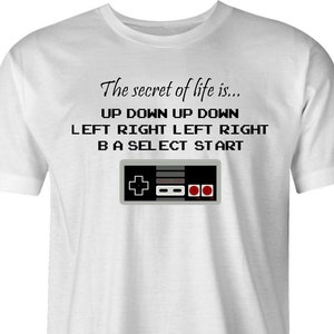 Könnte beinhalten: Weißes T-Shirt mit einem Grafikdruck eines Vintage-Videospiel-Controllers und dem Text "The secret of life is... UP DOWN UP DOWN LEFT RIGHT LEFT RIGHT BA SELECT START".