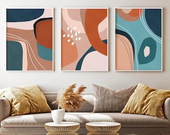 May include: Three abstract art prints with geometric shapes in shades of blue, brown, pink, and white. The prints are framed in white and hung on a white wall above a light brown sofa.