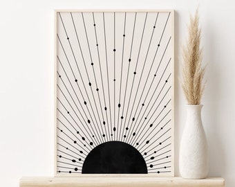 May include: A black and white minimalist art print of a sun with rays emanating from it. The print is framed in a light wood frame and is displayed on a wooden shelf.