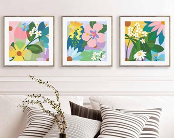 May include: Three framed prints with abstract floral designs in shades of pink, yellow, green, blue, and white. The prints are arranged in a row on a white wall.