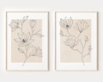 Puede incluir: Dos impresiones minimalistas de arte de línea de flores de magnolia sobre un fondo beige. Las impresiones están enmarcadas en un marco de madera claro.