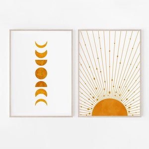 May include: Two framed prints with a minimalist design. The print on the left shows the phases of the moon in a vertical line. The print on the right shows a stylized sun with rays emanating from it. Both prints are in shades of yellow and orange.