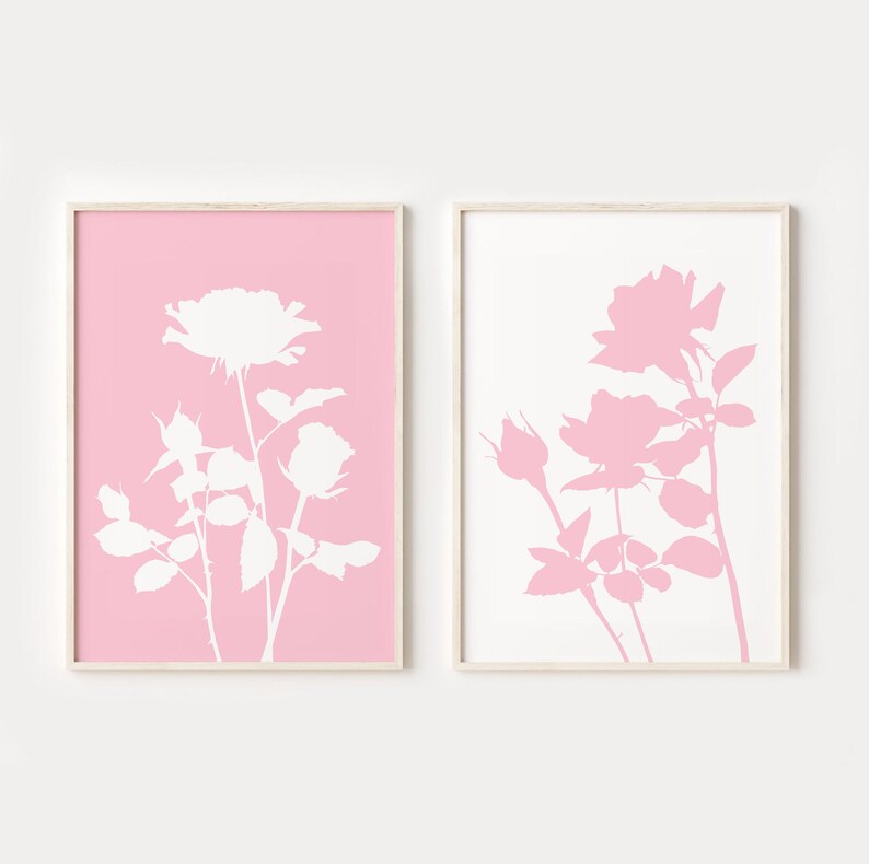 May include: Two framed prints with a pink and white color scheme. The prints feature a silhouette of a rose bush with white roses on a pink background and pink roses on a white background.