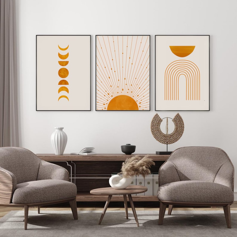 May include: Three minimalist wall art prints with a beige background and gold accents. The prints feature a sun with rays, a crescent moon with phases, and a rainbow arch.