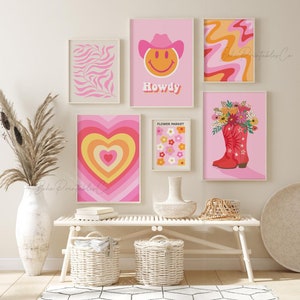 May include: A gallery wall with six framed prints in a pink and orange color scheme. The prints feature a smiley face with a cowboy hat, a heart with concentric circles, a flower market, a floral bouquet in a red cowboy boot, a pink and orange swirl pattern, and a pink and white leaf pattern.