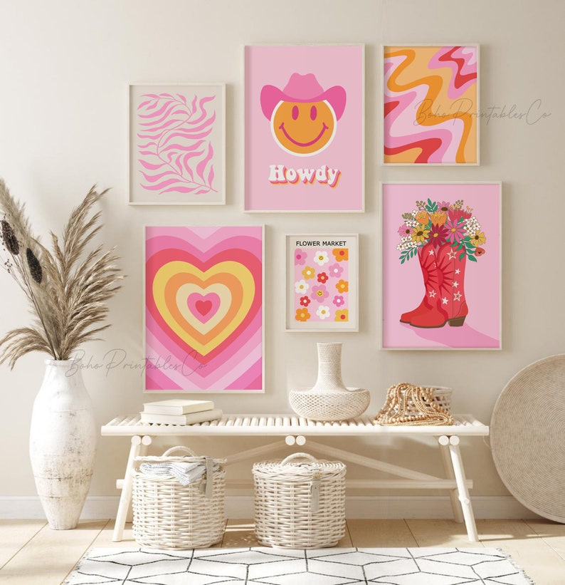 May include: A gallery wall with six framed prints in a pink and orange color scheme. The prints feature a smiley face with a cowboy hat, a heart with concentric circles, a flower market, a floral bouquet in a red cowboy boot, a pink and orange swirl pattern, and a pink and white leaf pattern.
