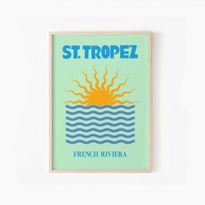 May include: A framed print with a blue and yellow illustration of a sun setting over the ocean. The text "ST. TROPEZ FRENCH RIVIERA" is printed below the illustration.