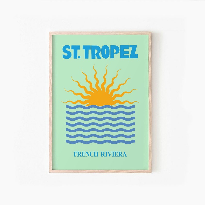 May include: A framed print with a blue and yellow illustration of a sun setting over the ocean. The text "ST. TROPEZ FRENCH RIVIERA" is printed below the illustration.